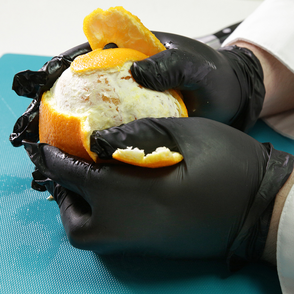 Peeling an orange while wearing Gloveworks Industrial Black Synthetic Hybrid Vinyl Gloves.