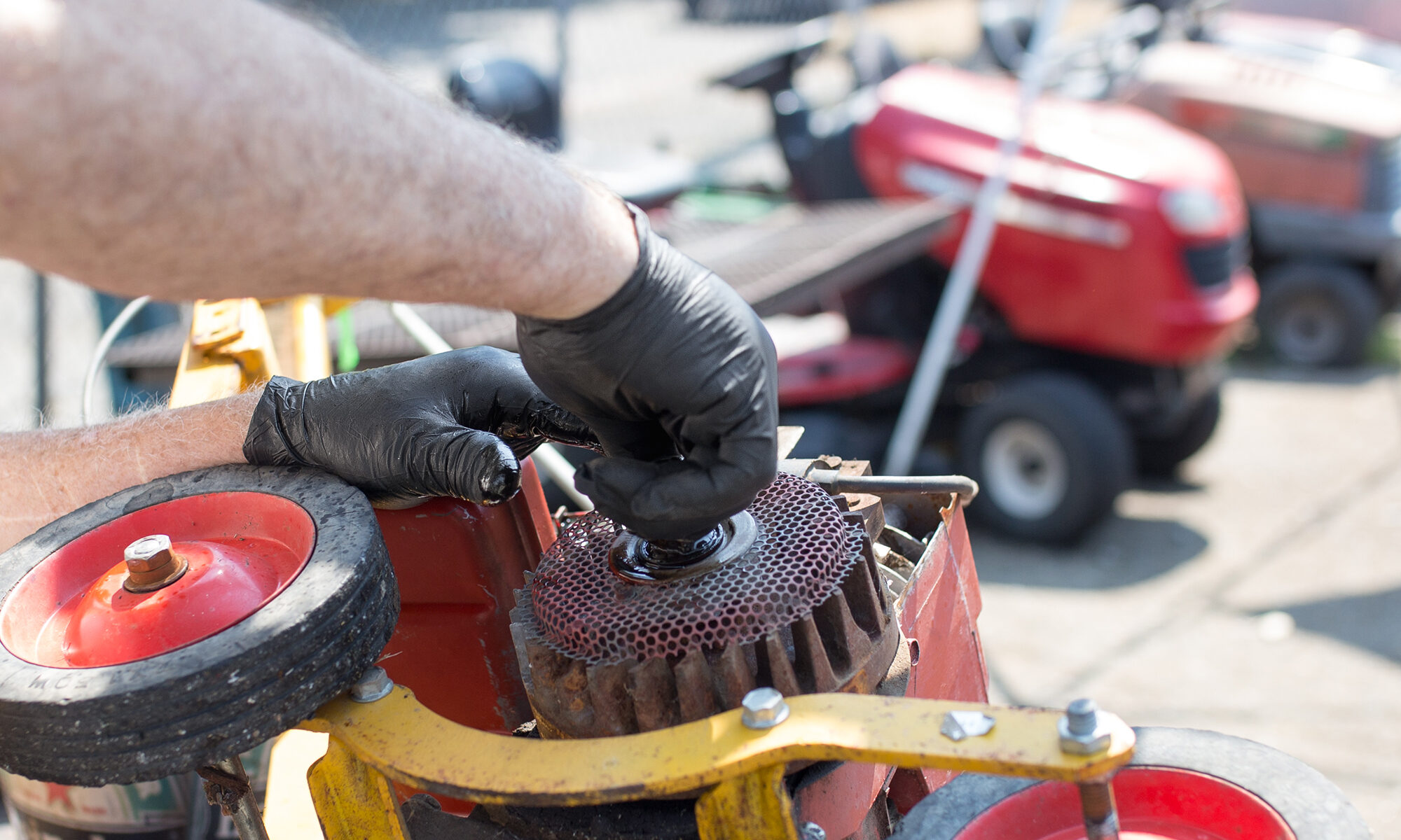 A man works on a lawnmower while wearing X3 Industrial Black Nitrile Gloves (BX3) from AMMEX.