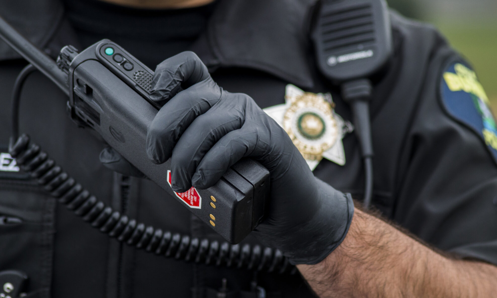 A law enforcement officer wears Gloveworks black nitrile gloves while holding a walkie talkie.