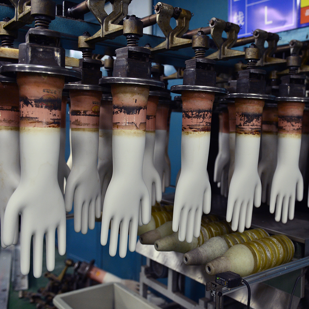 Disposable glove formers hang down from the production line.
