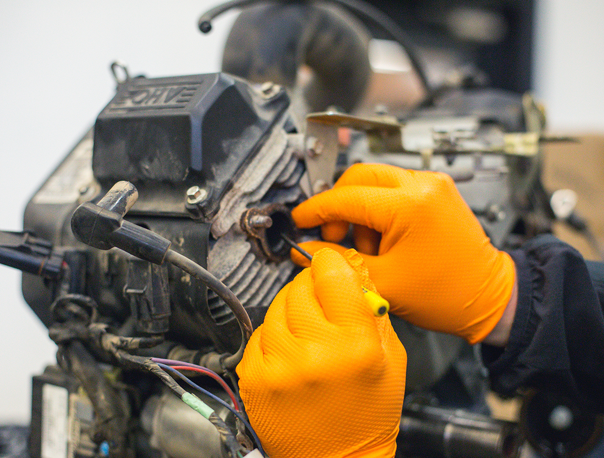 A mechanic works on an engine while wearing orange nitrile gloves from Gloveworks.