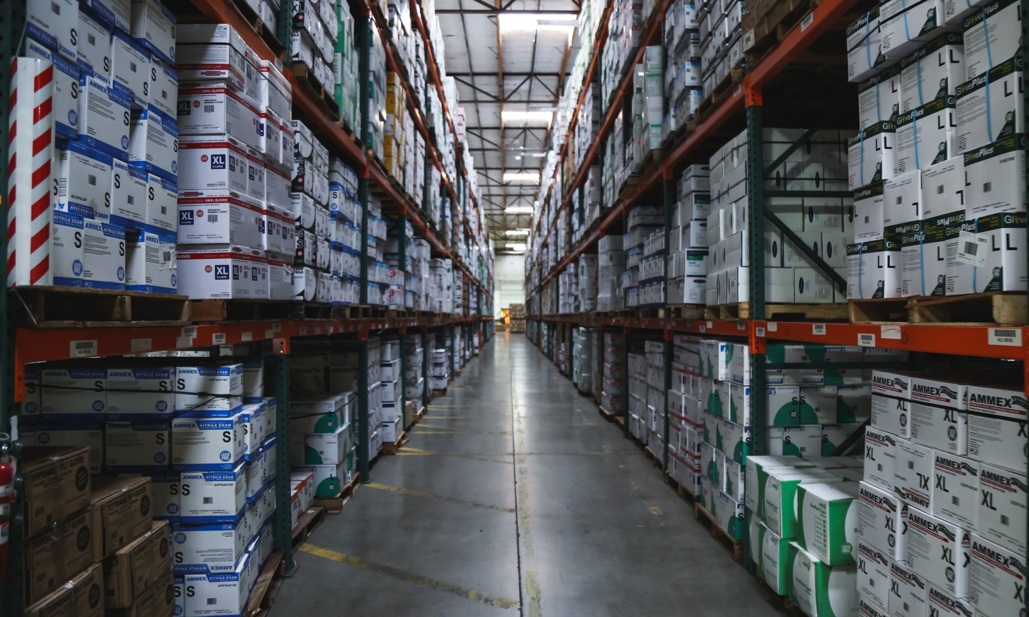 Cases of gloves line an aisle in a warehouse.
