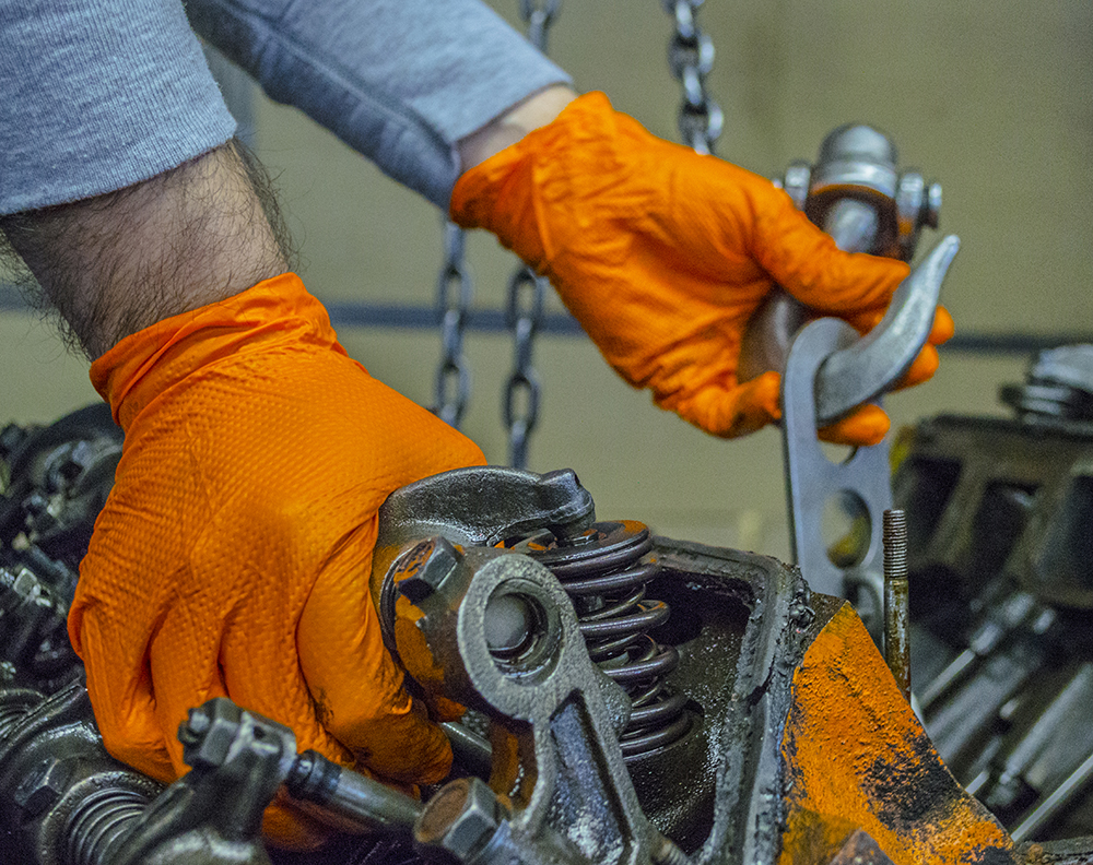 A worker wearing orange nitrile gloves from Gloveworks works with machinery.
