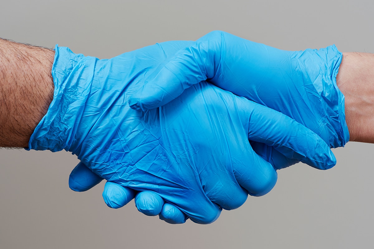 Two people shake hands while wearing blue nitrile disposable gloves.