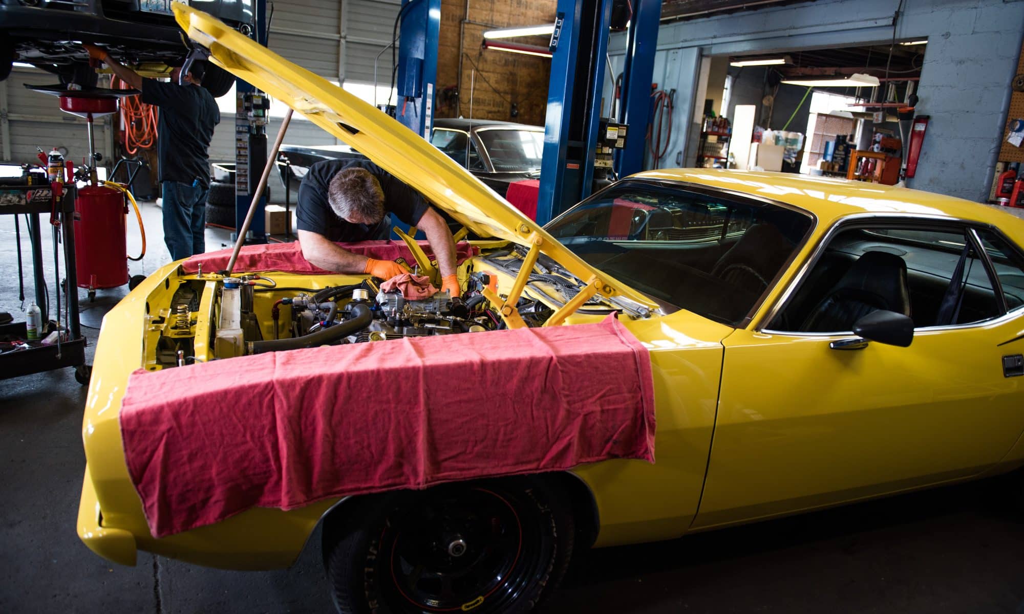 An automotive tech works on a yellow car in a garage.