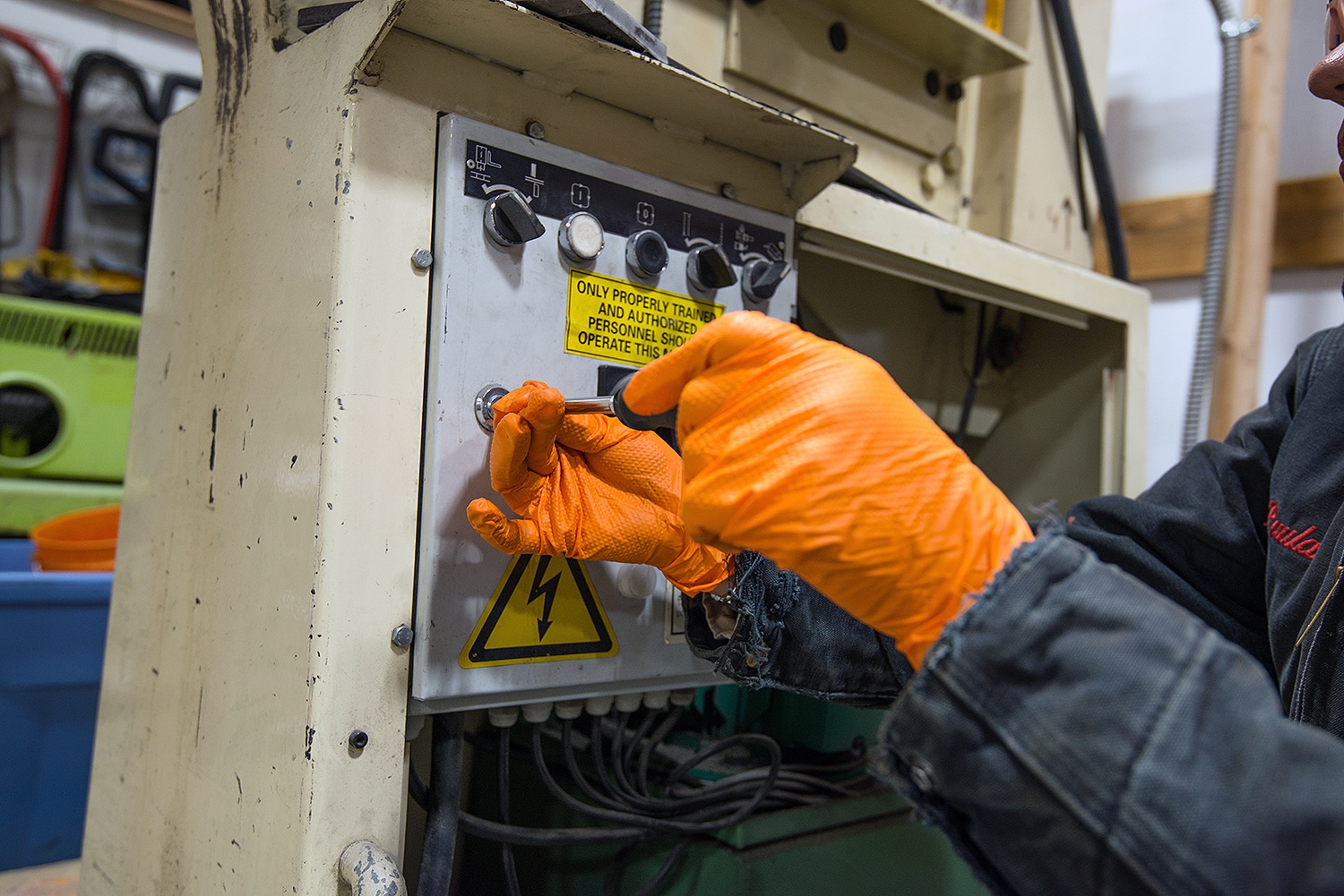 A worker wearing orange nitrile gloves from Gloveworks adjusts a machine.