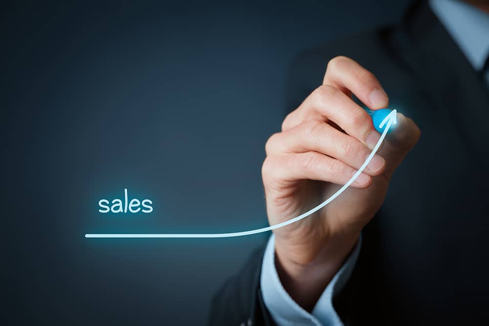 A hand draws an upward curve that reads "Sales."