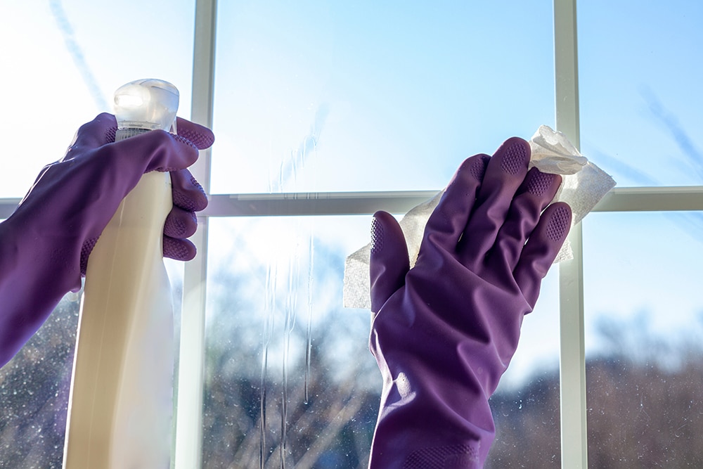 A worker wearing indigo gloves washes a window.